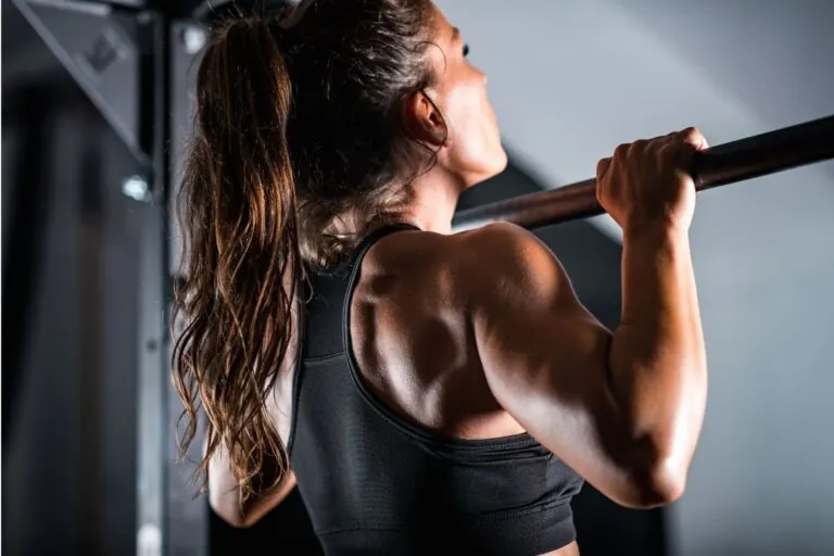 A woman with a ponytail doing the chin-up pull-up exercise.