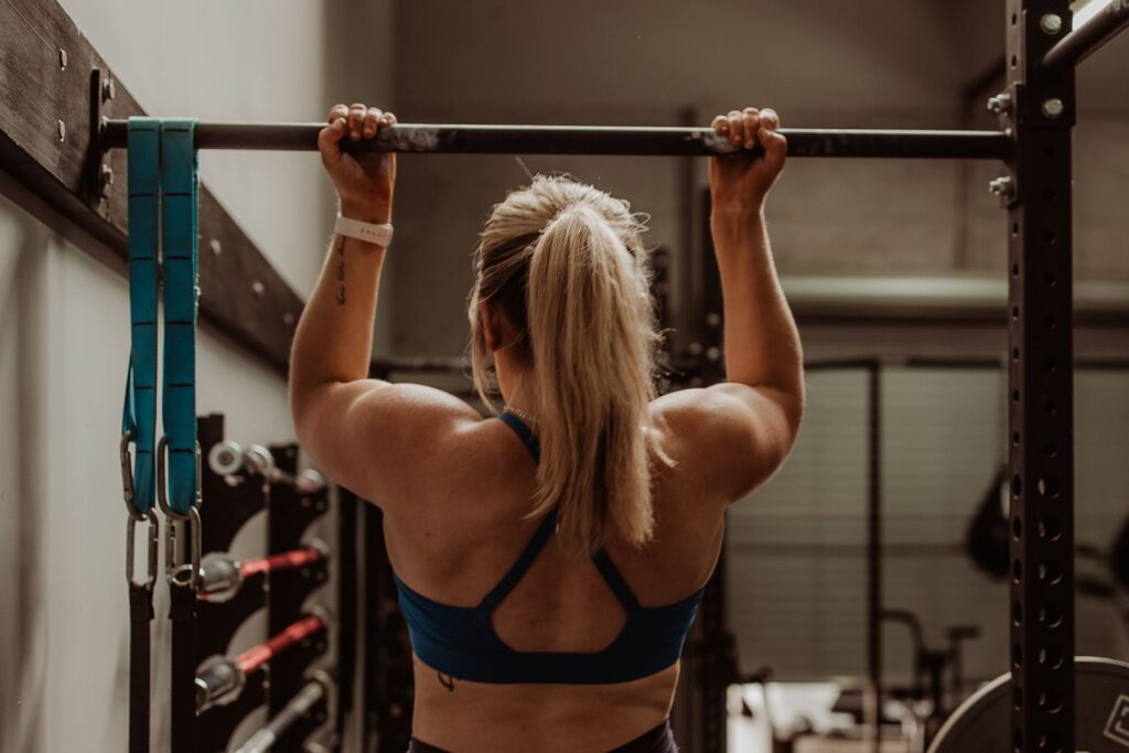 A woman with a ponytail and sports bra doing pull-ups at a fitness center.