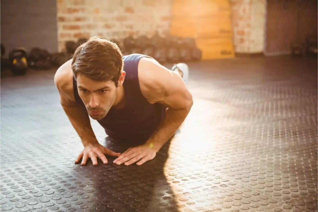 A man doing the diamond push-up exercise on a flat surface. Kettlebells are in the background.