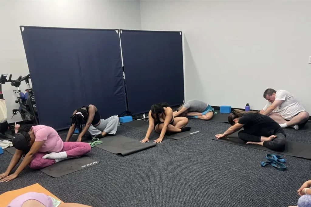 Six people performing the seated forward fold yoga pose in a room.